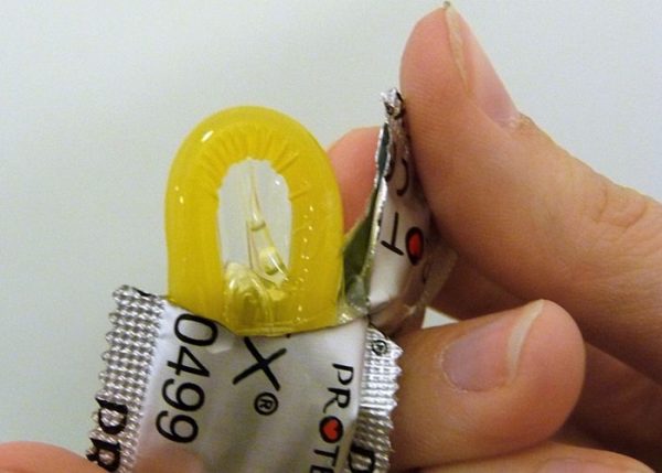 Открывает упаковку с презервативом