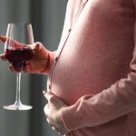 Беременная женщина держит в руках бокал вина