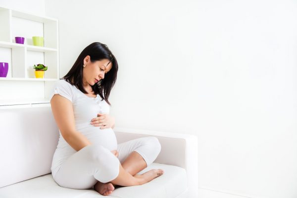 Беременная женщина в позе лотоса на белом диване