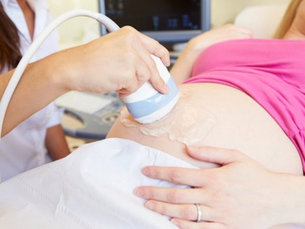 Рука врача водит аппаратом УЗИ по животу беременной женщины, которая находится в положении лёжа