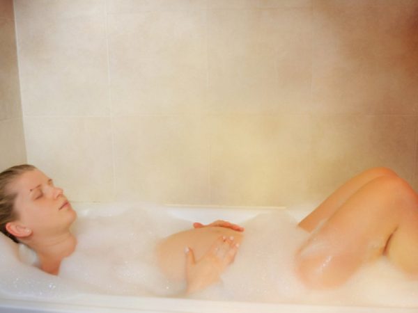 Беременная женщина с закрытыми глазами лежит в ванне с пеной