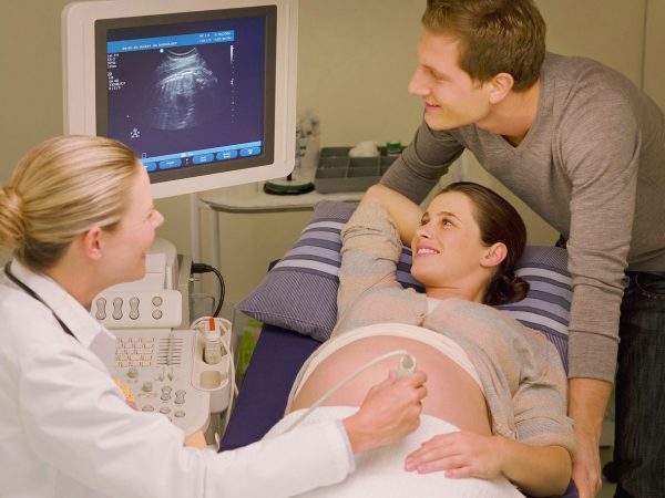 Беременная женщина и мужчина на процедуре УЗИ, рассматривают изображение на мониторе