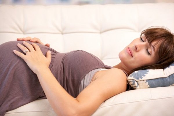 Беременная женщина с большим животом лежит на спине, закрыв глаза