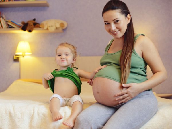 Беременная женщина с маленькой девочкой сидят на кровати