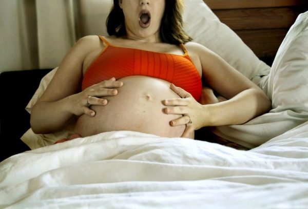 Беременная хватается за живот и раскрывает рот от удивления