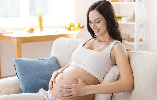 Беременная женщина идит на диване и держится за живот