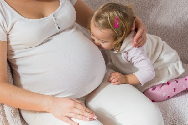 Беременная женщина с маленькой девочкой сидят на диване