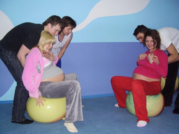 Занятие для будущих родителей по подготовке к родам: беременные сидят на фитболе, а мужья поддерживают их сзади