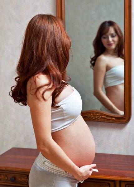 Беременная смотрит в зеркало на свой живот