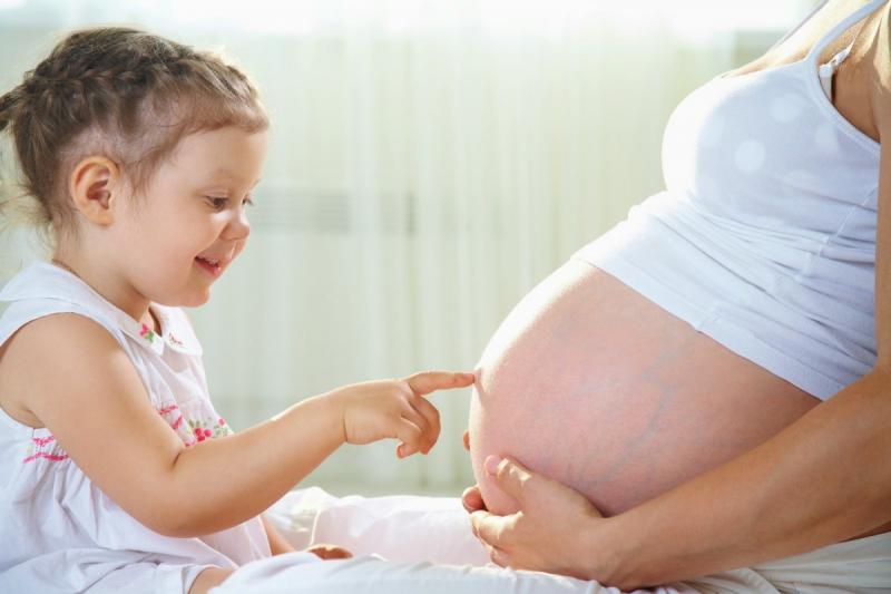 Девочка трогает живот беременной мамы