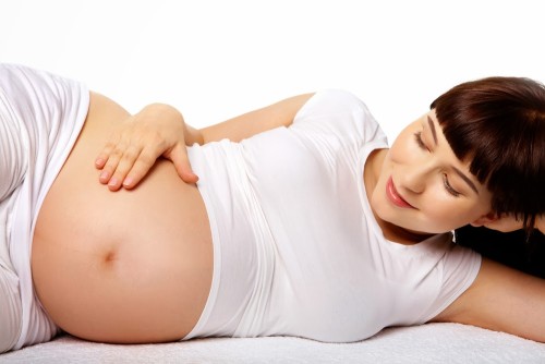 Фотография беременной женщины, лежащей на боку и смотрящей на свой живот