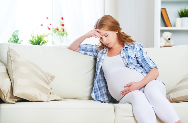 беременная сидит на диване, поддерживая рукой голову