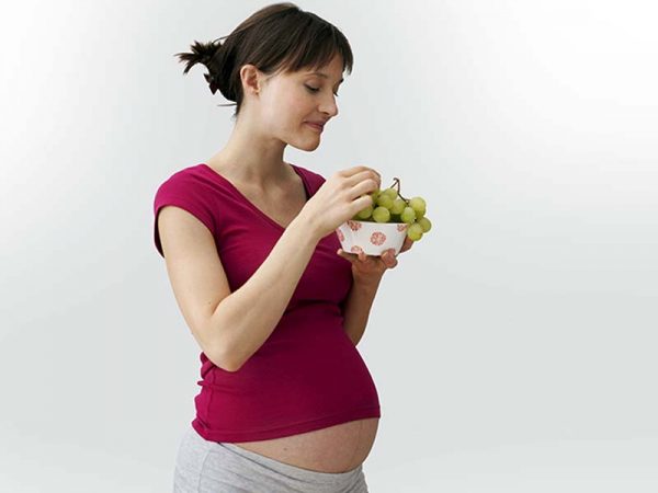 беременная держит чашку с виноградом