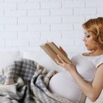 Беременная полулёжа на диване читает книгу