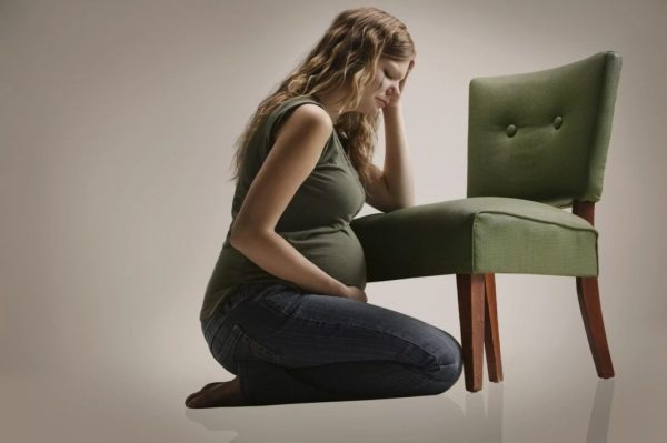 грустная беременная сидит на коленях, держась за голову