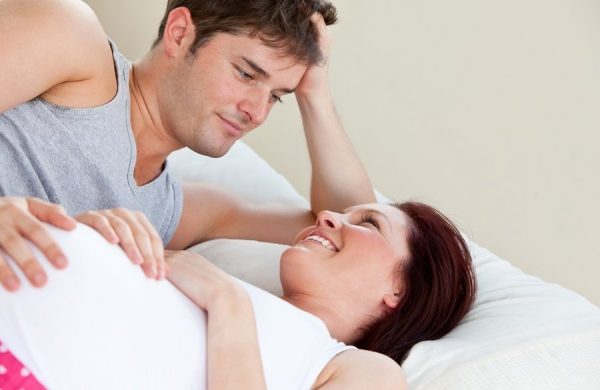 Беременная женщина лежит с мужем в постели и улыбается