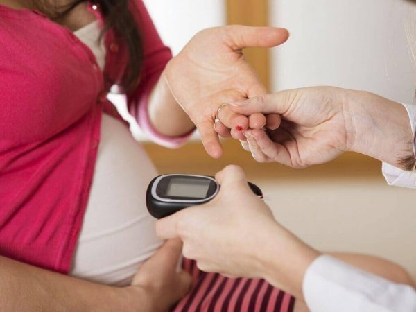 Рука держит руку беременной женщины с кровью на безымянном пальце, вторая рука держит глюкомер