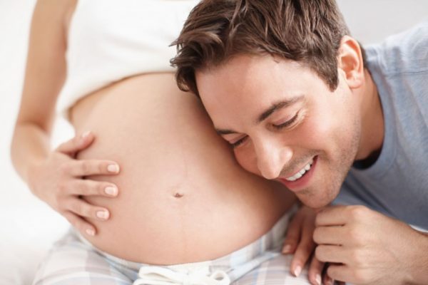 Улыбающийся мужчина прижимается ухом к животу беременной