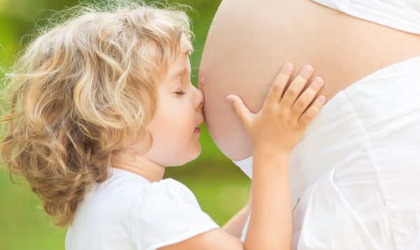 Кудрявый ребёнок уткнулся носом в беременный живот мамы и обнял его руками