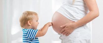 Мальчик в тельняшке упирается кулачками в беременный живот мамы