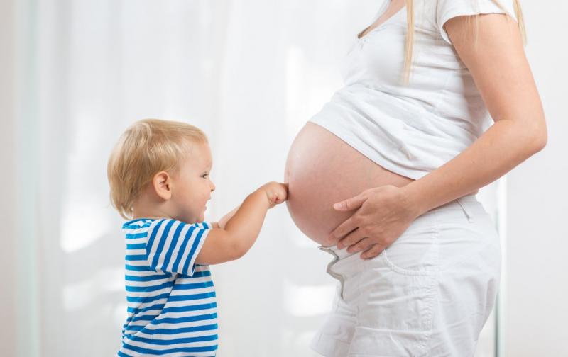 Мальчик в тельняшке упирается кулачками в беременный живот мамы