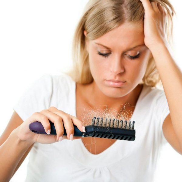 Девушка смотрит на расчёску с прядями волос