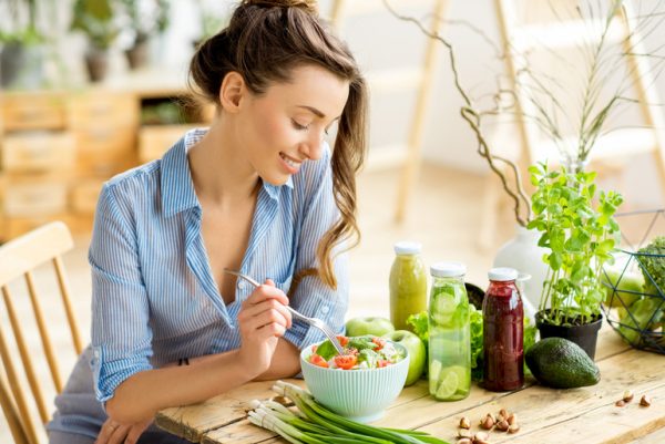 Женщина сидит за столом и ест салат из овощей