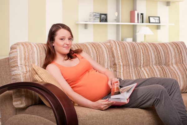 беременная полулежит на диване, в руках книга