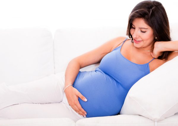 Беременная женщина улыбается и гладит свой живот