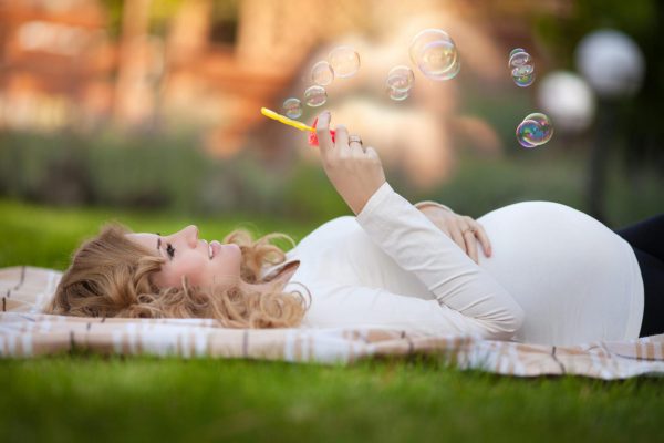 Беременная женщина лежит и пускает мыльные пузыри