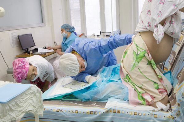 Беременная стоит на коленях, рядом — врачи