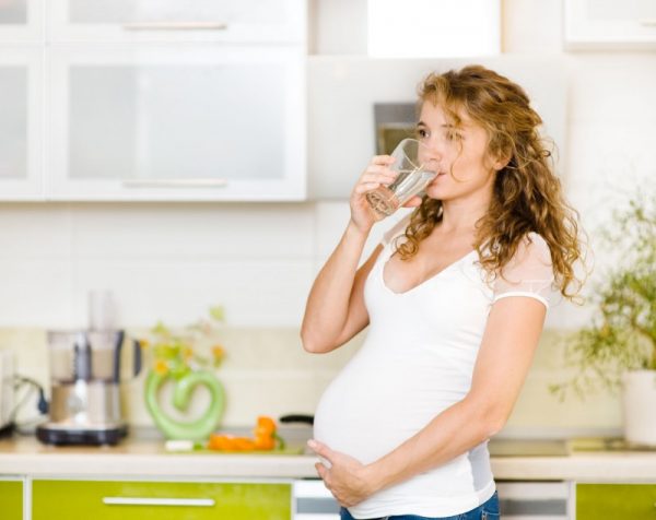 беременная на кухне пьёт воду из стакана