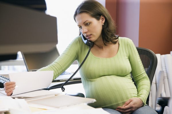 Беременная женщина разговаривает по телефону и смотрит документы